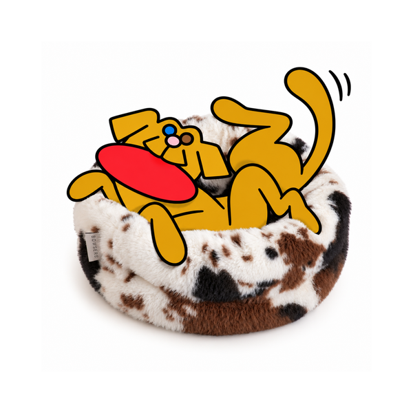 Bowsers Muffy dog bed in cowhide print with the illustrated Fetch dog playfully tumbling inside with a red frisbee.